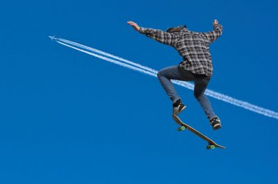 A teenager skateboards with the contrails of a jet in the background