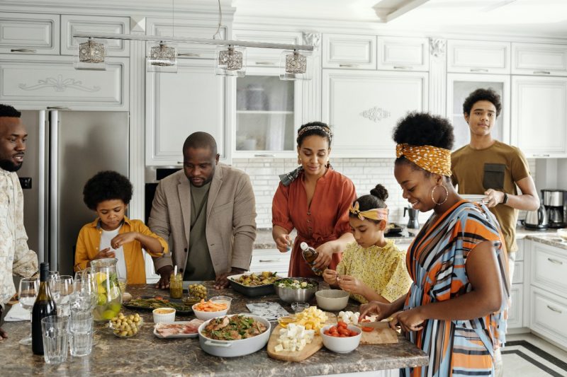 Family members gather around a kitchen counter preparing food. Photo by August de Richelieu.