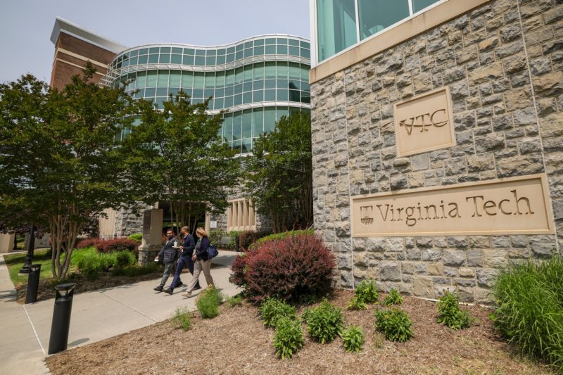Three people walk along the sidewalk outside the front entrance to the Virginia Tech Carilion School of Medicine building in Roanoke, VA.