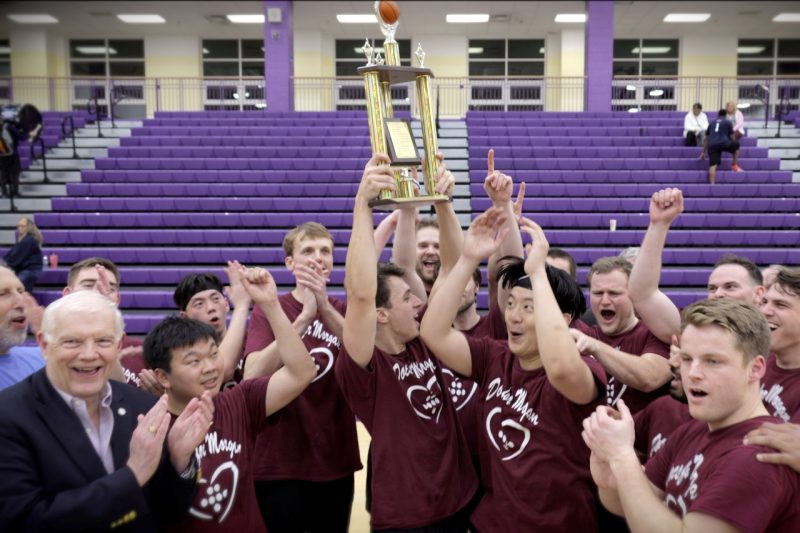 Smiling and screaming medical school students lift a trophy above their heads.