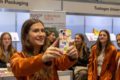 A group of college-aged women take a photo in front of an event booth.