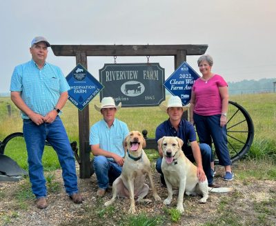 A family and their dogs stand in front of a farm sign.