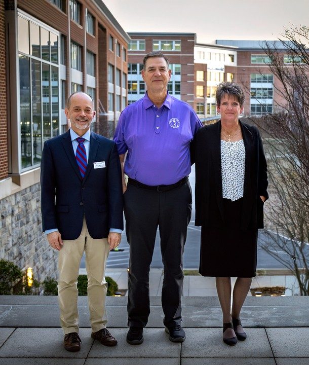 Two men and a woman stand together in front of buildings. 