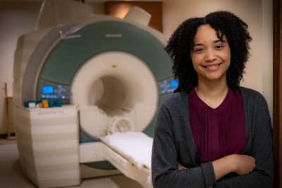 Woman standing with arms folded and MRI machine in background