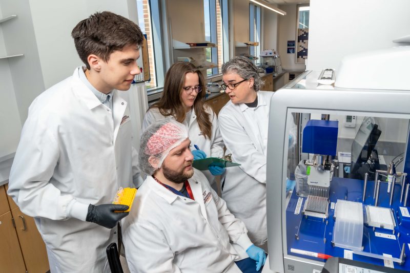 Virginia Tech researchers John Janiga, Dzenis Mahmutovic (seated), Katherine Brown, and lead investigator Carla Finkielstein work together in the Molecular Diagnostics Laboratory 